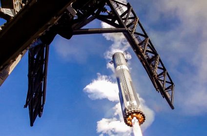 SpaceX Starship Super Heavy booster lifting off from launch tower with active Raptor engines and grid fins deployed for test flight